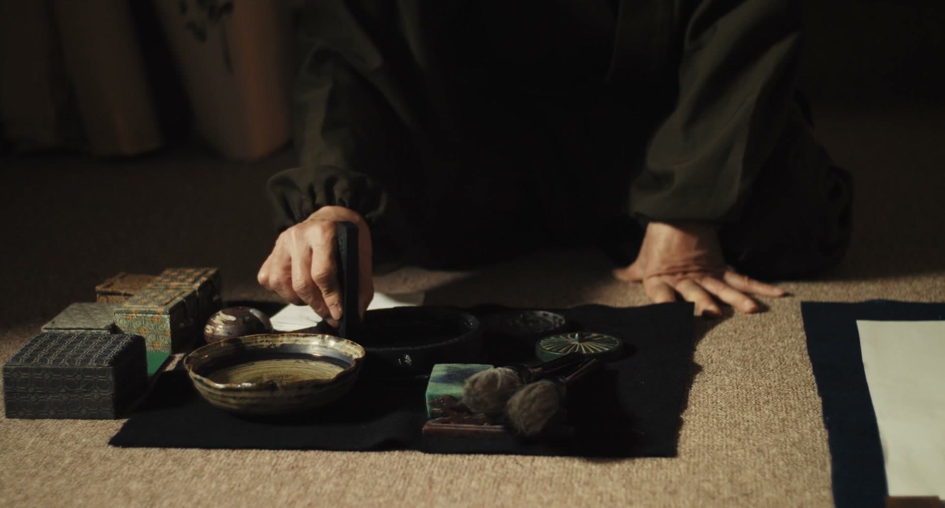 A calligrapher at a low table, grinding ink